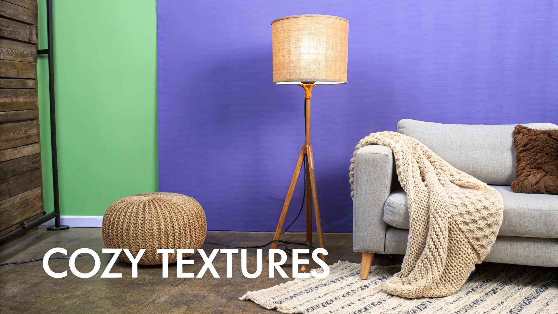 A cozy living room featuring a grey couch, knitted blanket, pouf, and warm wooden floor lamp.