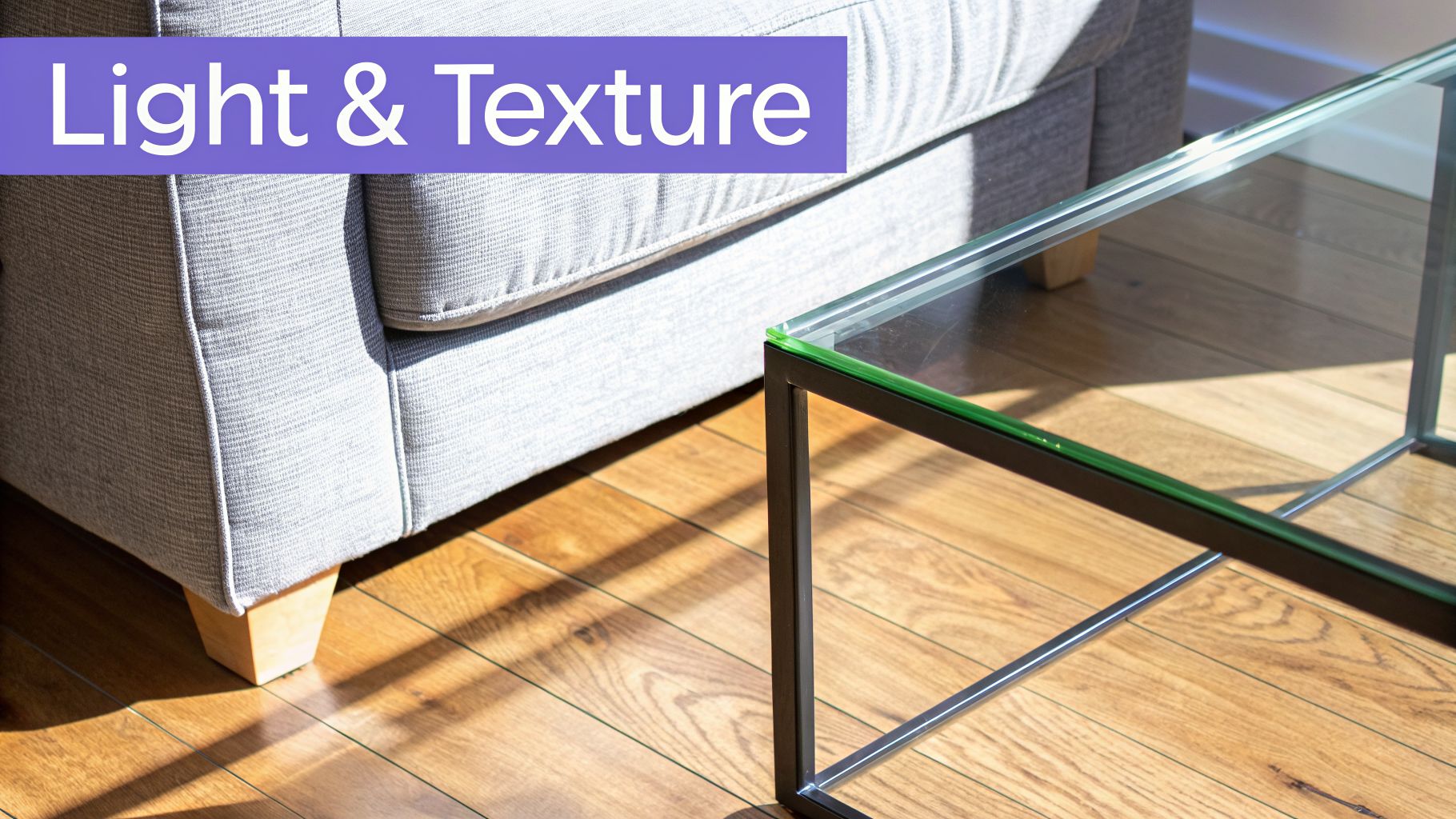 Close-up of a light grey sofa, a glass coffee table, and a wooden floor with sunlight.